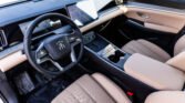 Luxury car interior: beige leather seats, large touchscreen infotainment, and a round steering wheel with a badge in a sleek dashboard.