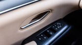 Car interior door panel with beige upholstery and a chrome door handle next to window and mirror controls on a black console area