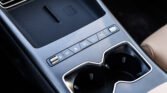 Close-up of a car center console showing assorted control buttons and a textured area, with two cup holders on the right edge and chrome trim nearby.