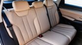 Beige leather car back seats with three headrests and visible seat belts and door panel.