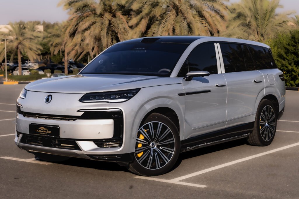 White luxury SUV/van parked in a sunny outdoor lot with palm trees in the background, showing the front and side profile.