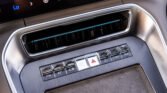 Close-up of a car center console: horizontal air vent with chrome surround and a row of glossy control buttons below, including the hazard light button.