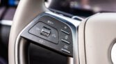 Close-up of a car steering wheel control panel with Japanese labels and a central rocker switch on beige leather trim.