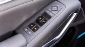 Close-up of a car door armrest with power window switches and a square mirror-adjustment pad on gray leather trim used by the driver side