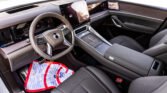 Luxurious car interior with a leather steering wheel, large touchscreen display, and wood-grain dashboard center console visible from the passenger side.