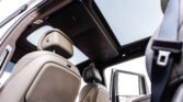 Beige leather car interior with rows of seats and a panoramic sunroof seen from the back seat area.
