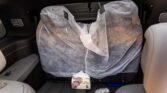 Backseat of a car with protective plastic seat covers and a small patterned package resting on the seat cushion.