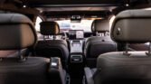 Rear-seat perspective of a modern SUV interior with a central touchscreen and driver area visible through the windshield, sunroof overhead.