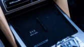 Close-up of a car's center console showing a wireless charging pad labeled MAX 50W, surrounded by beige leather and chrome trim.