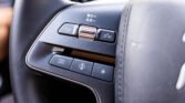 Close-up of a car steering wheel with a silver roller and two side buttons, with white text on the panel above in a dark interior scene.