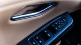Close-up of a car door window control panel on a beige interior, showing multiple window buttons and a circular mirror-control pad beside it.