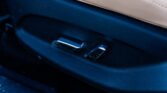 Close-up of a car seat buckle latch on dark blue upholstery with a beige seam above.