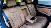 Tan leather back seat of a car with three headrests, seat belts, and center cupholders.