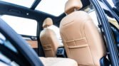 Interior of a car with tan leather seats and a panoramic sunroof, viewed from the rear passenger area.