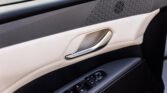 Beige car door interior with a chrome handle and a row of window and mirror control buttons on a dark panel.