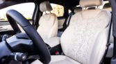 Front interior of a car with light beige perforated leather seats and a black steering wheel in the foreground