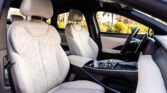 Beige leather car seats and center console inside a car, with greenery visible through the windows outside.
