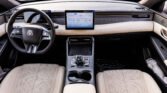 Interior of a luxury car with beige seats, two digital screens on the dashboard, and a steering wheel with controls.
