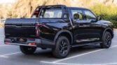 Rear-left view of a glossy black pickup truck with a cargo rack parked in a lot, palm trees in the background.