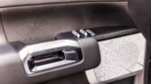Close-up of a car door interior showing a textured panel, chrome door handle, and three small silver switch controls on the armrest.
