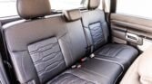 Rear passenger seats in a black leather car interior with headrests and seat belts