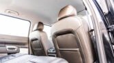 Rear car passenger area with beige leather seats and headrests, showing the backseat and open door.