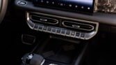 Car interior center console with a large touchscreen and row of metallic buttons below the dash.