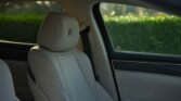 Beige leather car seat and headrest with an XR logo, view of a green hedge through the window.