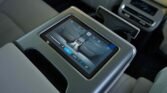 In-car rear-seat control panel with a touchscreen displaying climate controls and seat icons.