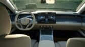Interior of a futuristic car with a large central touchscreen, light-colored seats, and a minimalist dashboard.