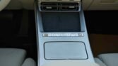 Center console of a car interior with a brushed metal surface, storage tray, and a row of small control buttons across the front.