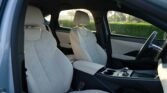 Interior of a modern car with light beige leather seats, center console, and steering wheel visible in the cabin edge view.