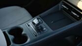 Center console of a car featuring a glossy gear shifter, cup holders, and control buttons nearby.