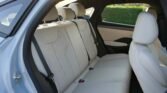 Back seat of a white SUV with light beige leather upholstery and three headrests, rear door open nearby.