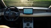 Interior of a modern car cabin with a digital instrument cluster behind the steering wheel and a large tablet-style central touchscreen on the dash; center console with gear shifter visible.