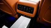 Rear center console in a tan leather car interior with an illuminated climate-control panel and a lower open storage tray.