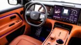 Luxurious car interior with orange leather seats and dashboard, large touchscreen display on the center console, and a black steering wheel.