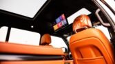 Orange leather car interior with a ceiling-mounted entertainment screen and sunroof glass, front seat visible