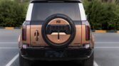 Rear view of a bronze SUV with a full-size spare tire mounted on the tailgate in a parking lot.