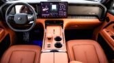 Front-seat view of a luxury car interior with orange leather seats, a wide touchscreen dashboard, and metallic accents on the console.