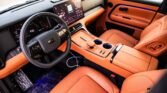 Luxury car interior with orange leather seats, a large digital dashboard and center touchscreen panel to the passenger side