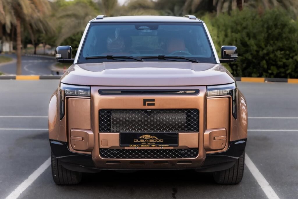 Front view of a copper-colored SUV in a parking lot, featuring a bold grille and rectangular headlights with a tall, boxy design.