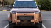 Front view of a copper-colored SUV in a parking lot, featuring a bold grille and rectangular headlights with a tall, boxy design.