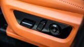 Orange leather car seat with electronic adjustment controls: two switches and a circular dial on a black panel.