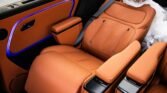 Orange leather car seats with perforated stitching and black center console armrests; blue ambient lighting along the door panel and armrest edge.