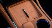 Center console of a brown leather car interior showing a wireless charging pad labeled MAX 50W and a nearby circular control dial with blue lighting.