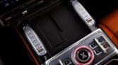 Center console of a luxury car with climate/seating controls, a prominent circular dial with red ring, and an NFC wireless charging pad in the middle.