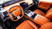 Luxurious car interior with bright orange leather seats, steering wheel, and center console featuring a large digital touchscreen display.