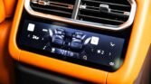Car interior with a digital climate control screen in orange trim; shows front-seat icons and temperature readout.