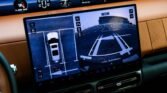 In-car infotainment screen showing a split view: top-down parking guide on left, rear camera view with parking lines on right, dashboard gauges above.